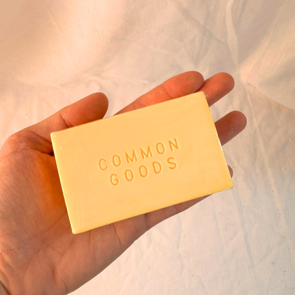 A bar of Red Palm Geranium handmade soap held in an open hand on cream cloth