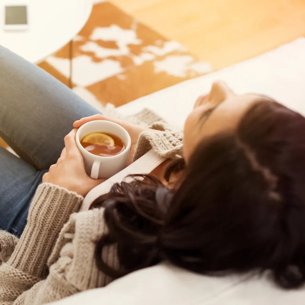Person resting on a sofa holding a warm cup of tea